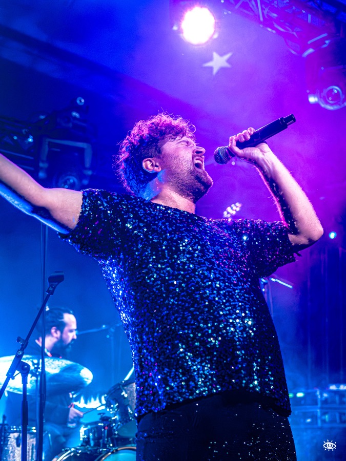 Frontmann David Lindermeier singt im Paillettenoutfit unter blauem Bühnenlicht.
