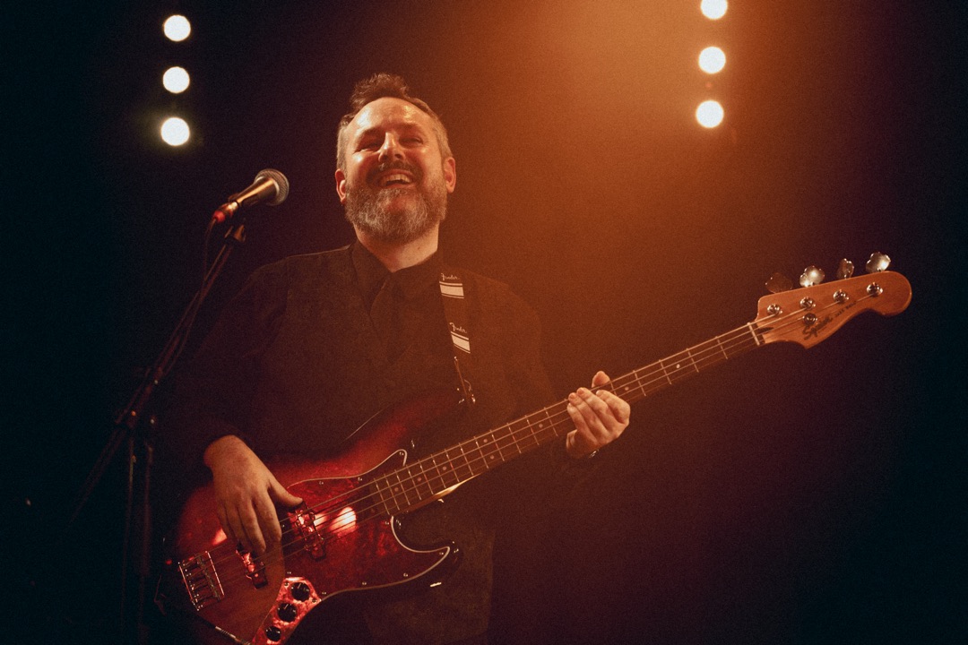 Martin lacht beim Bassspielen im warmen Bühnenlicht.